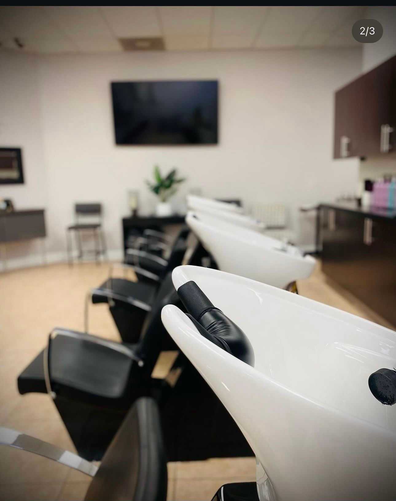 Modern salon with black and white washbasins, chairs, and a large wall-mounted TV.